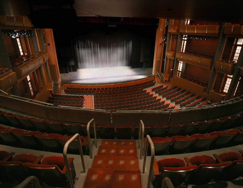 Empty theater auditorium with tiered seating facing a stage with closed curtains.